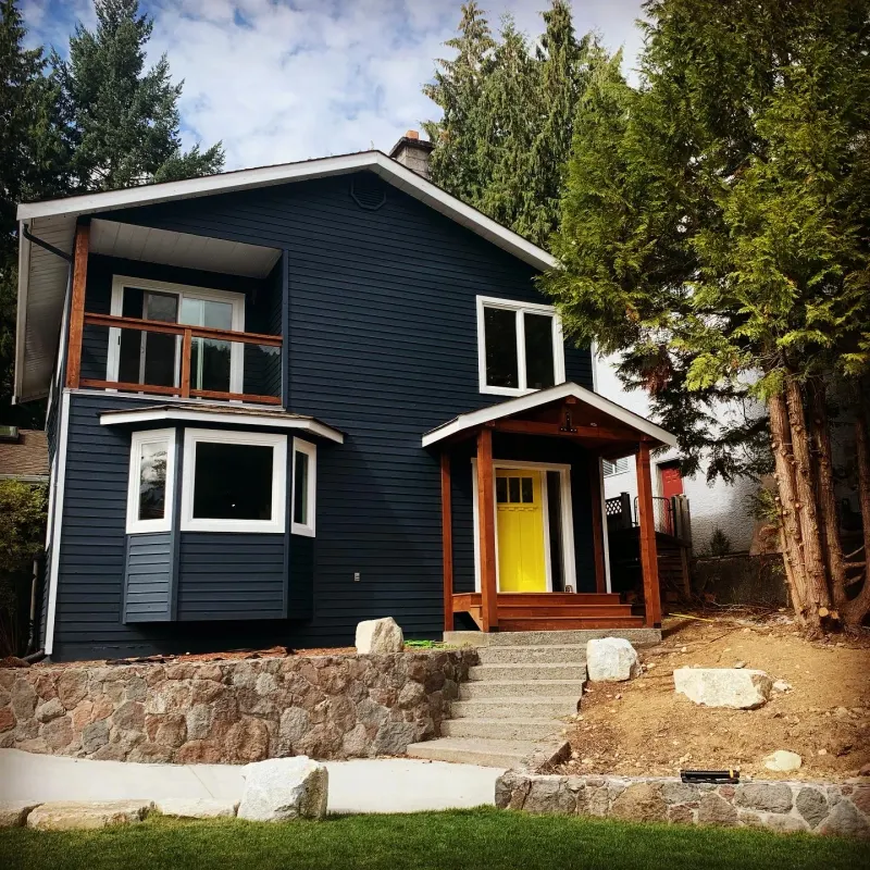 Completed exterior house painting in Squamish BC, navy siding with yellow door by Colour Craft Painting